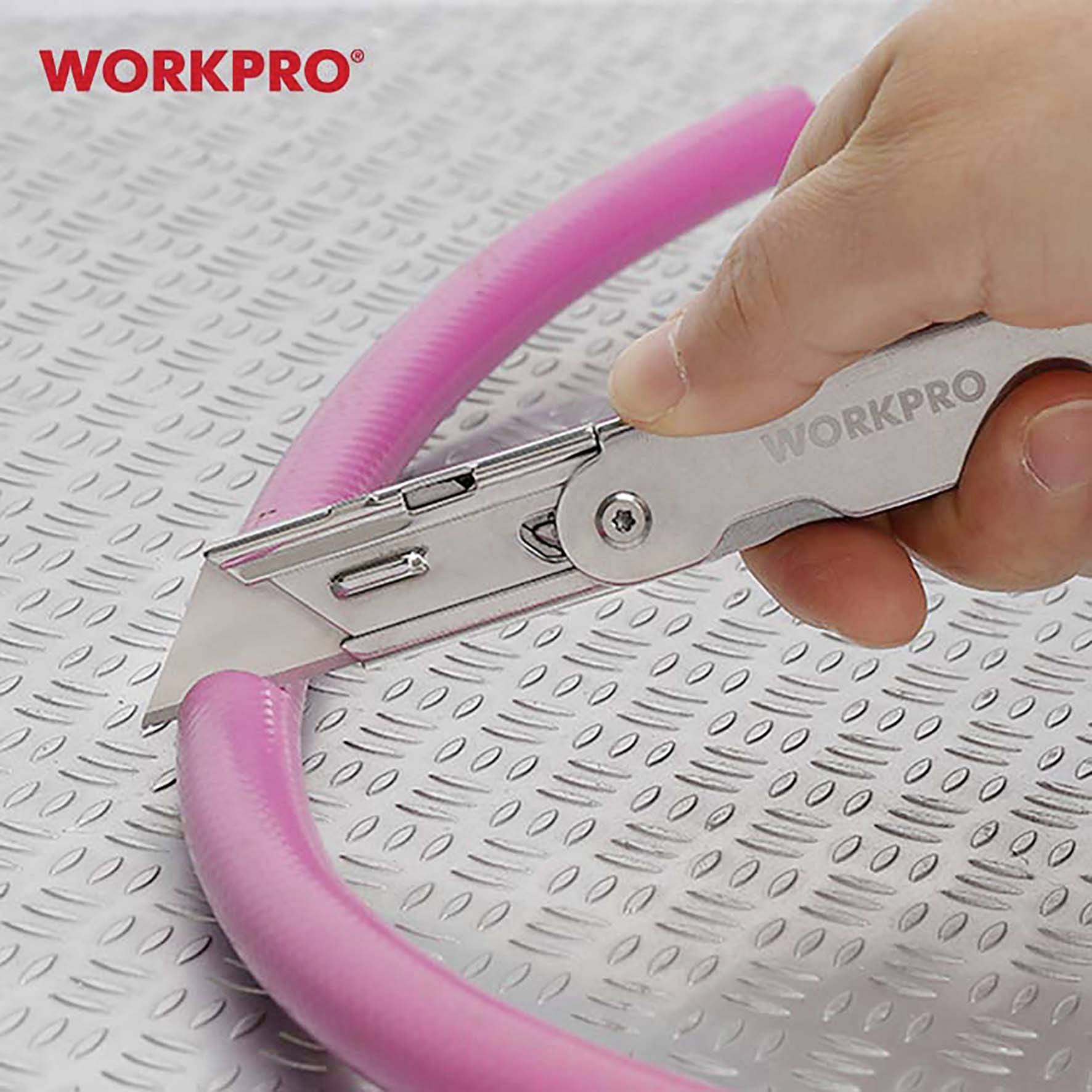 Une main tient un couteau universel WORKPRO argenté, qui coupe un tube en mousse rose sur une surface métallique cannelée.