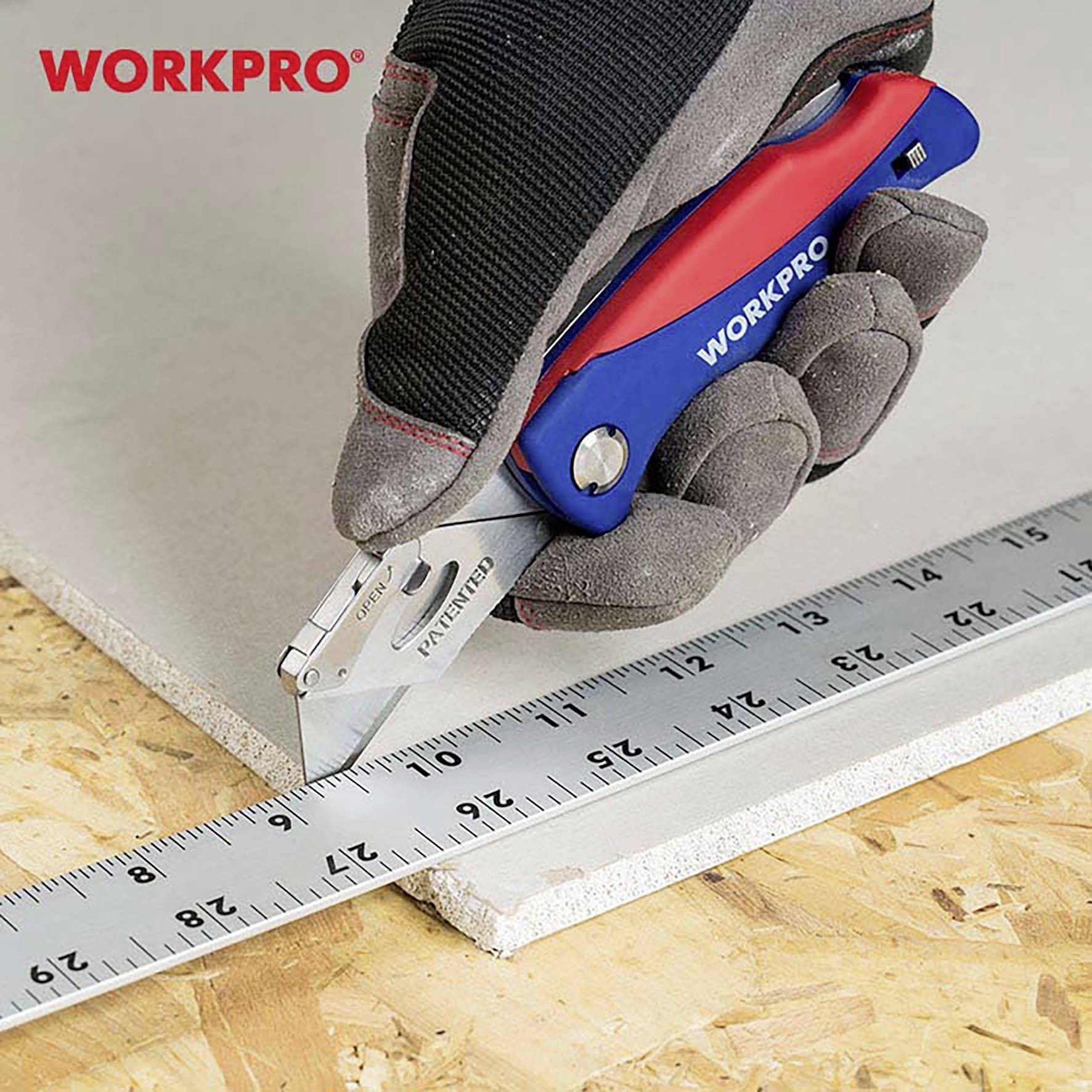 Une main gantée tient un couteau multifonction bleu et rouge de la marque 'WORKPRO', qui coupe une plaque de plâtre le long d'une règle métallique.