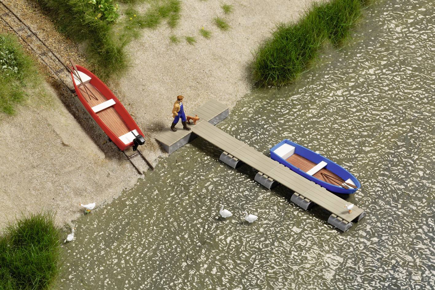 Un modèle miniature représente un homme sur une passerelle entre deux bateaux, entouré d'eau et d'herbes. Trois canards nagent dans l'eau.