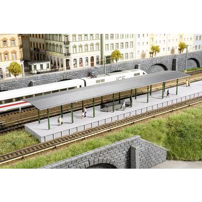 Scène de train miniature avec un train ICE sur les voies. Des passagers attendent sur le quai. Décor urbain environnant avec des bâtiments historiques.