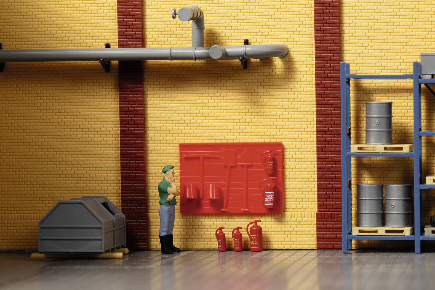 Une figurine miniature se tient dans une halle d'usine devant un mur équipé d'extincteurs et d'outils. Des étagères avec des tonneaux sont visibles en arrière-plan.