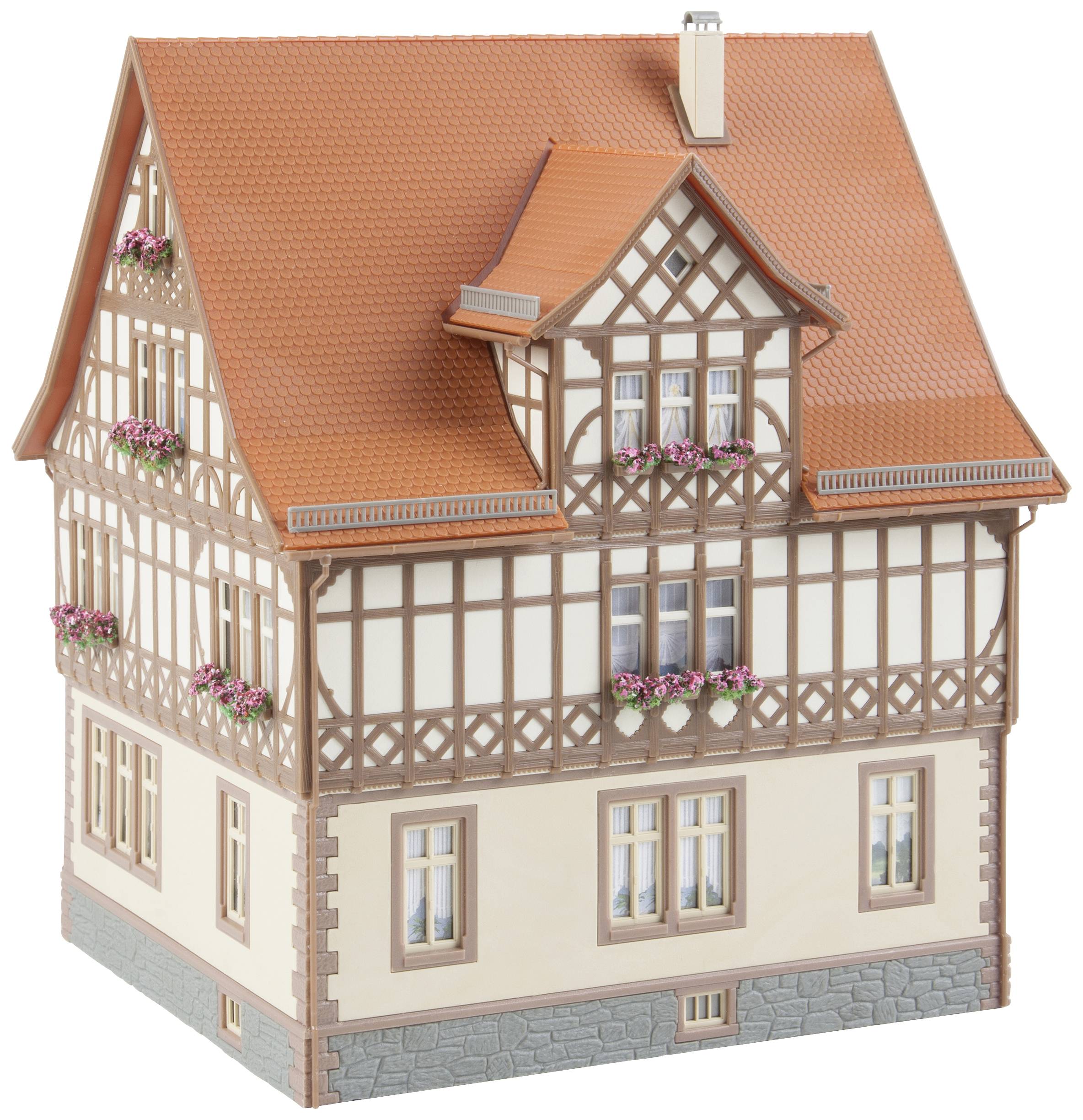 Modèle réduit d'une maison à colombages avec un toit pointu, plusieurs fenêtres et des jardinières de fleurs ; exemple d'architecture traditionnelle.