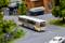 Un bus miniature à motif zébré roule sur une route miniature. Des arbres, une clôture et un camion sont visibles en arrière-plan.