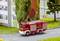 Une voiture de pompiers miniature roule sur une route miniature à côté d'un bâtiment à la façade colorée et des arbres en arrière-plan.