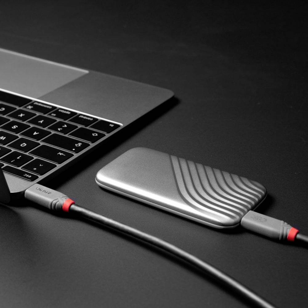 Un ordinateur portable est connecté à un disque dur externe via un câble USB. Les appareils sont posés sur une table noire.