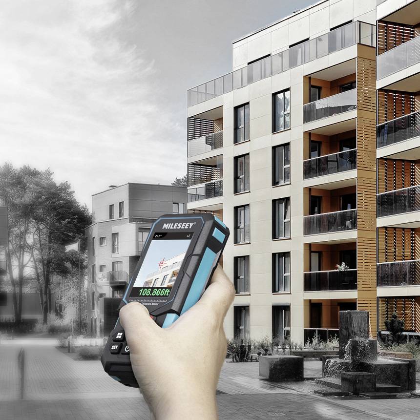 Une main tient un appareil de mesure numérique devant un immeuble résidentiel moderne à plusieurs étages.