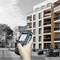 Une main tient un appareil de mesure numérique devant un immeuble résidentiel moderne à plusieurs étages.