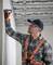 Un homme en tenue de travail et portant des lunettes de protection mesure un mur avec un télémètre laser dans une pièce inachevée.