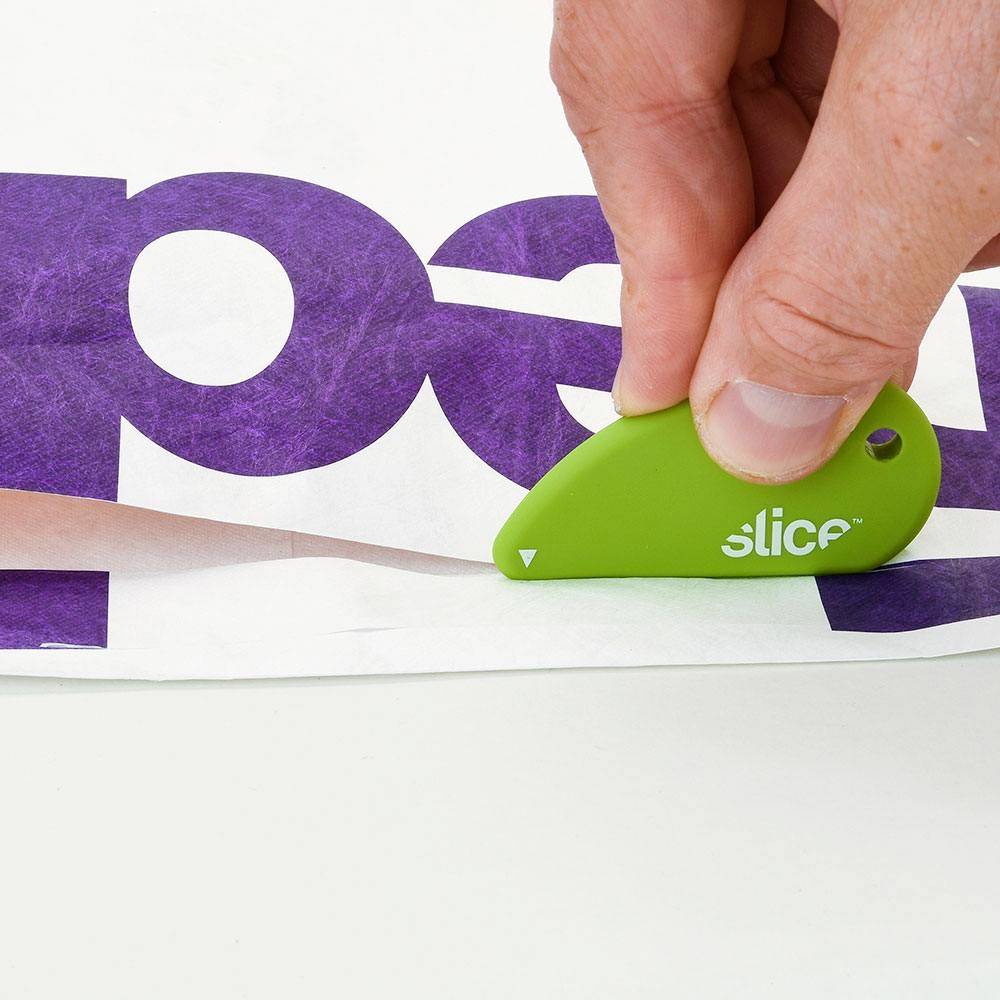 Une main coupe du papier avec un petit outil vert, portant un imprimé lilas.