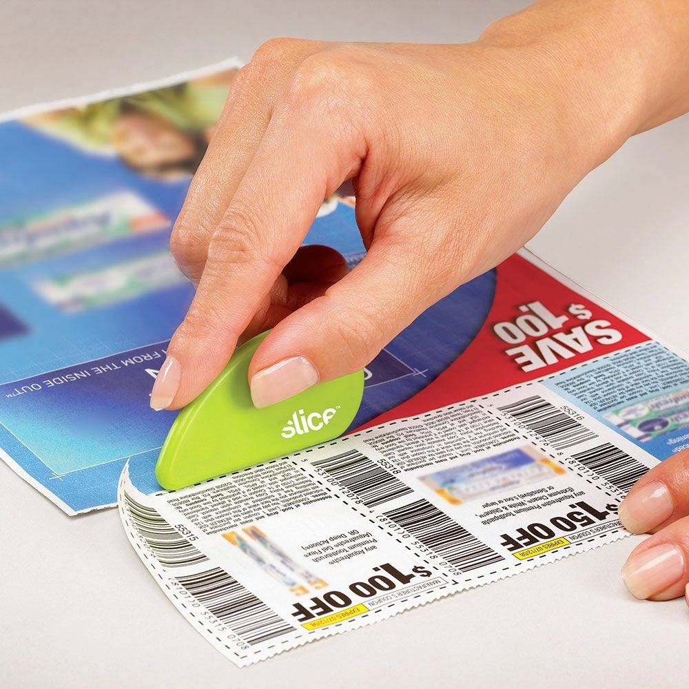 Une main découpe des coupons avec un petit appareil de découpe vert à partir d'un magazine.