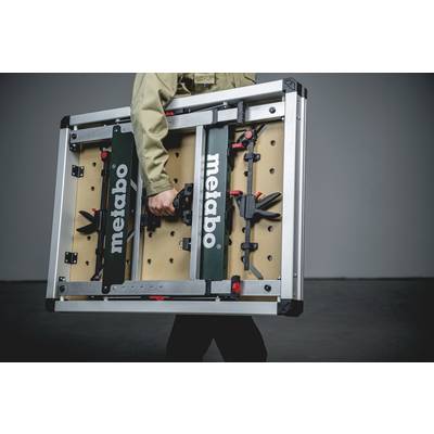 Une personne transporte une table de travail portable de la marque 'Metabo'. La table dispose d'un cadre métallique et est pliable.
