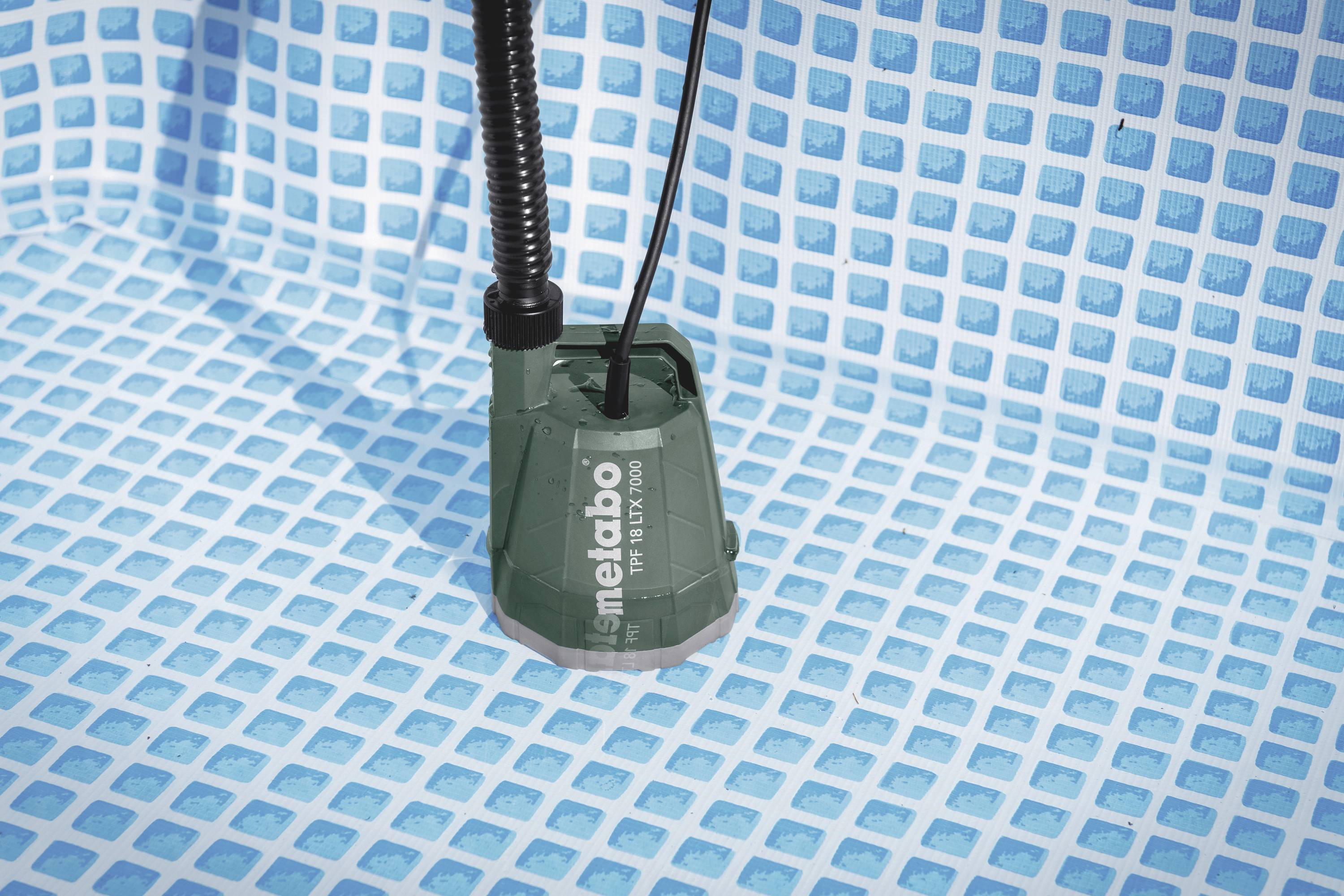 Pompe à eau verte dans une piscine bleue vide avec un motif de carrelage en damier au sol, portant un nom de marque.