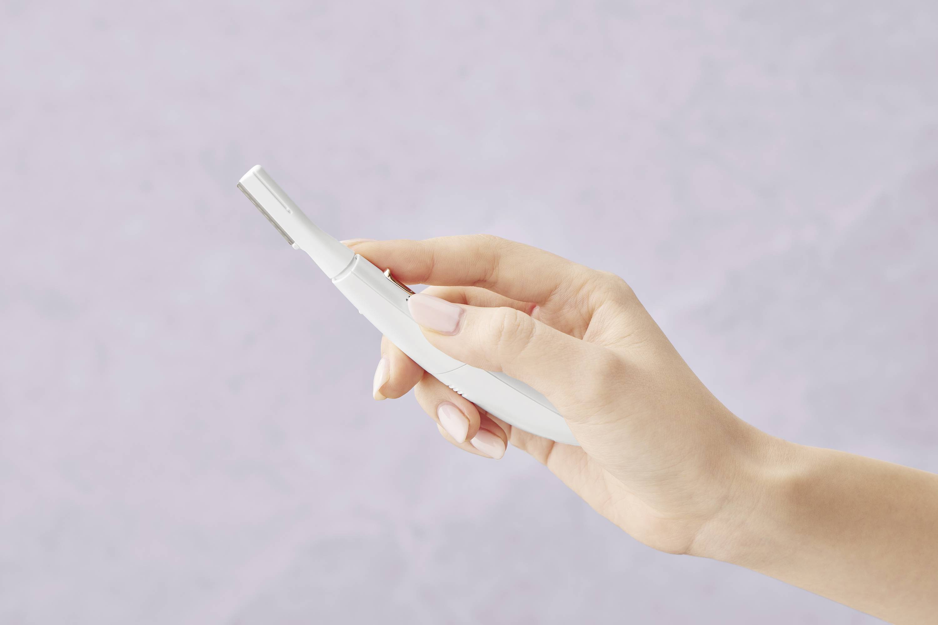 Une main tient une tondeuse à barbe électronique blanche devant un fond neutre violet clair.