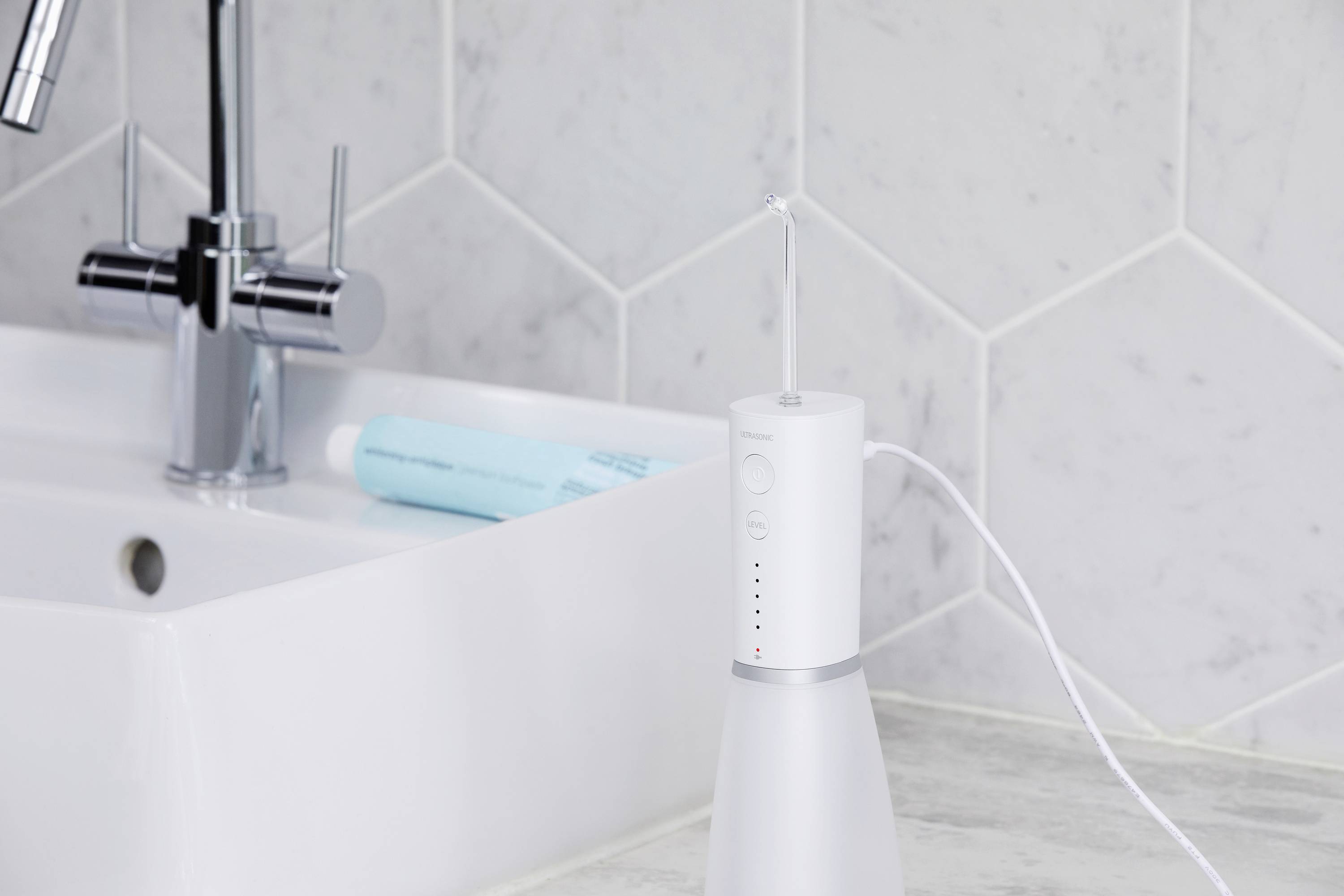 Une douche buccale électrique est posée à côté d'un lavabo dans la salle de bain, une bouteille d'eau étant visible.