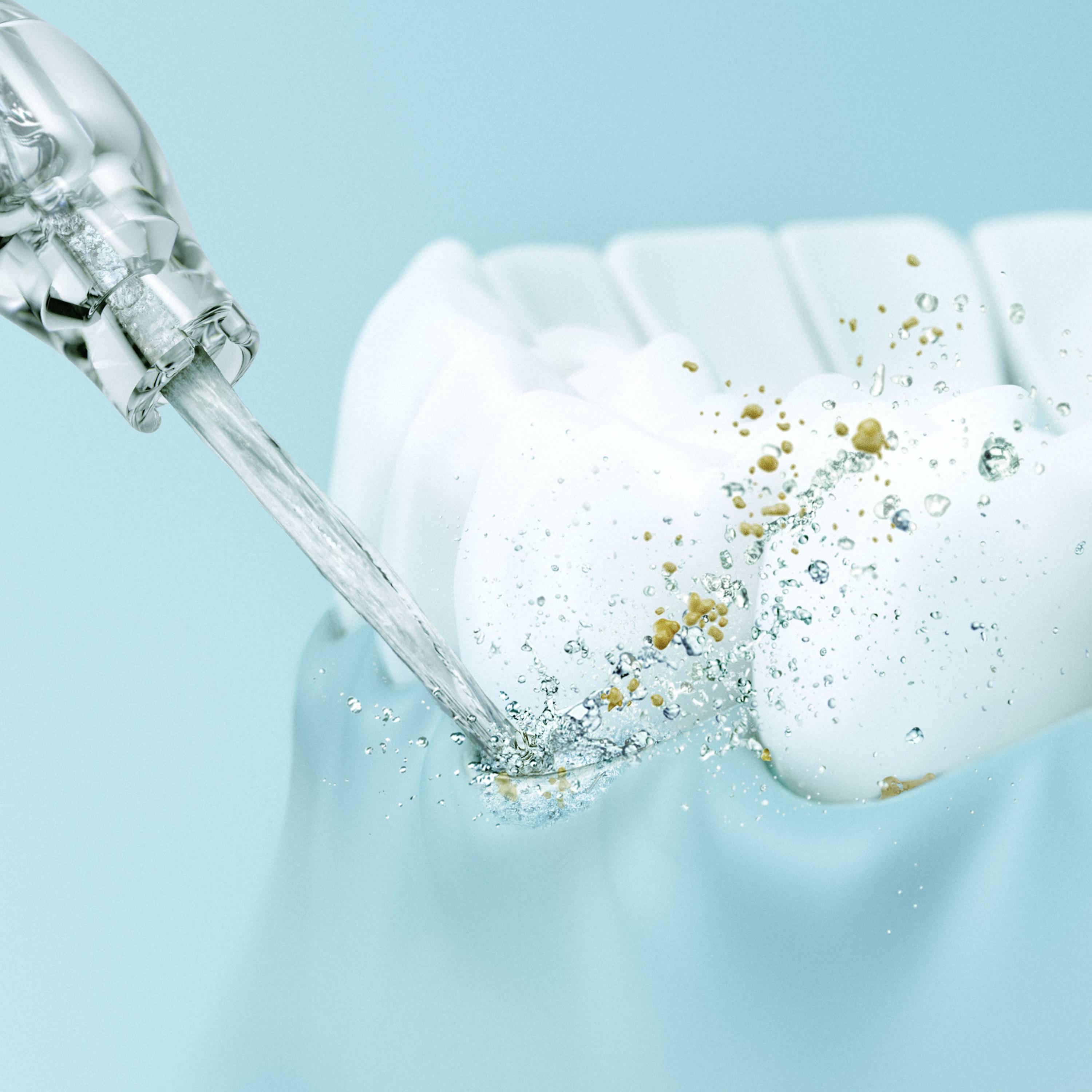 Gros plan d'une dent sur laquelle un jet d'eau de solution de nettoyage élimine des restes alimentaires et de la plaque dentaire.