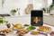 Un four de cuisine moderne sur un plan de travail, entouré de différents plats tels que du poulet rôti, des légumes et des petits pains.