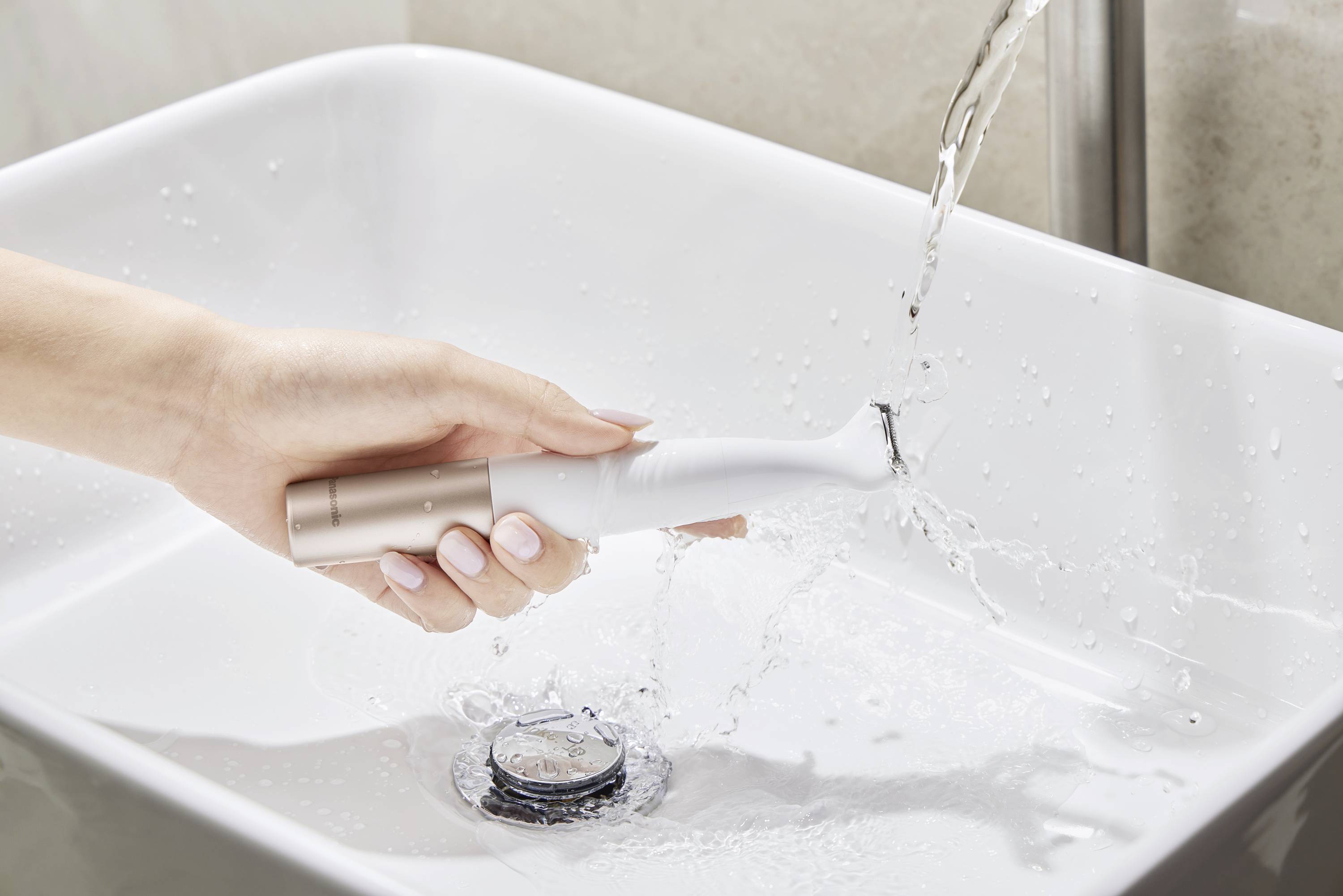 Une main tient une brosse à dents électrique sous l'eau courante au-dessus d'un lavabo.