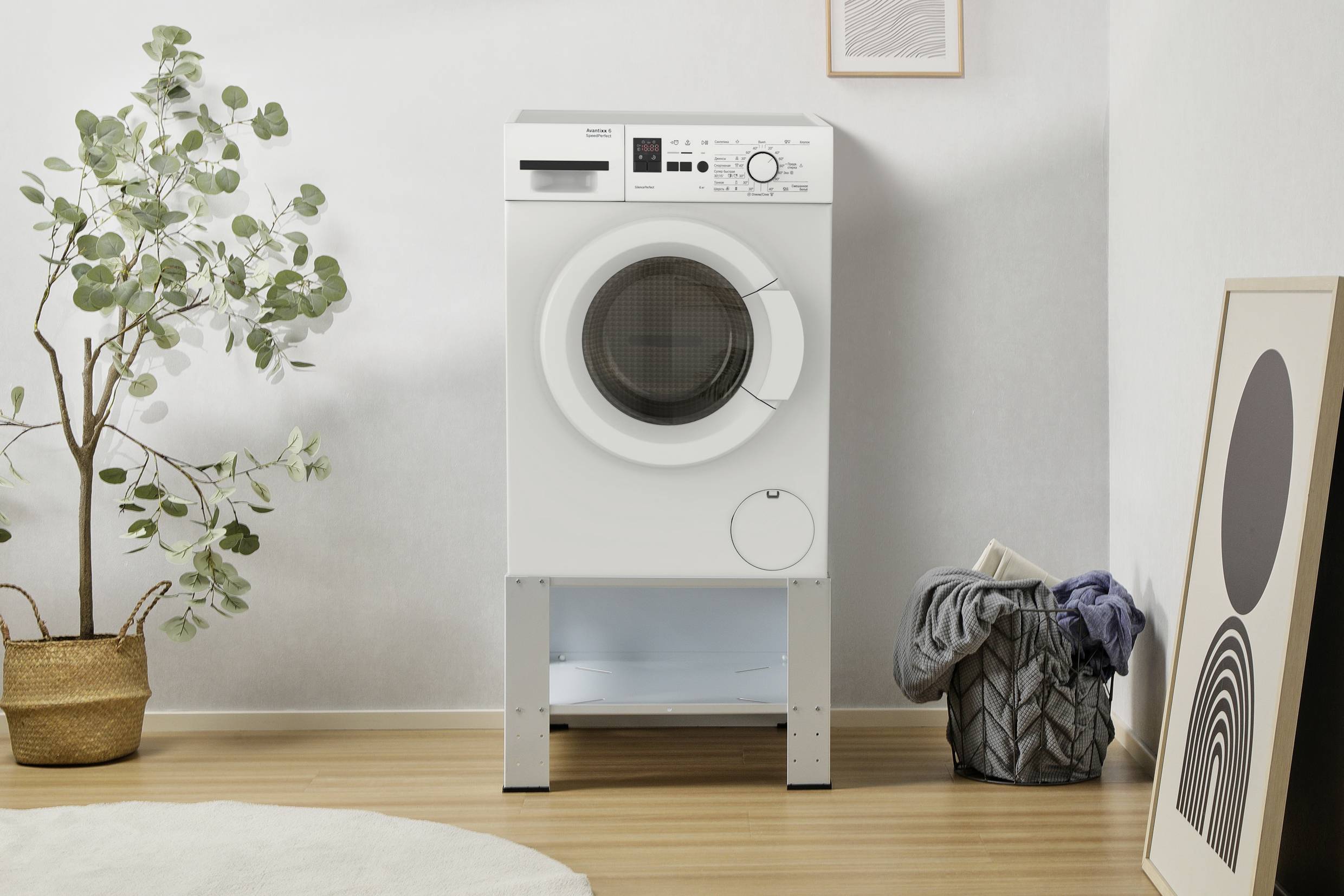 Machine à laver dans une pièce moderne, entourée d'un panier de linge et d'une plante. Aménagement simple et épuré.