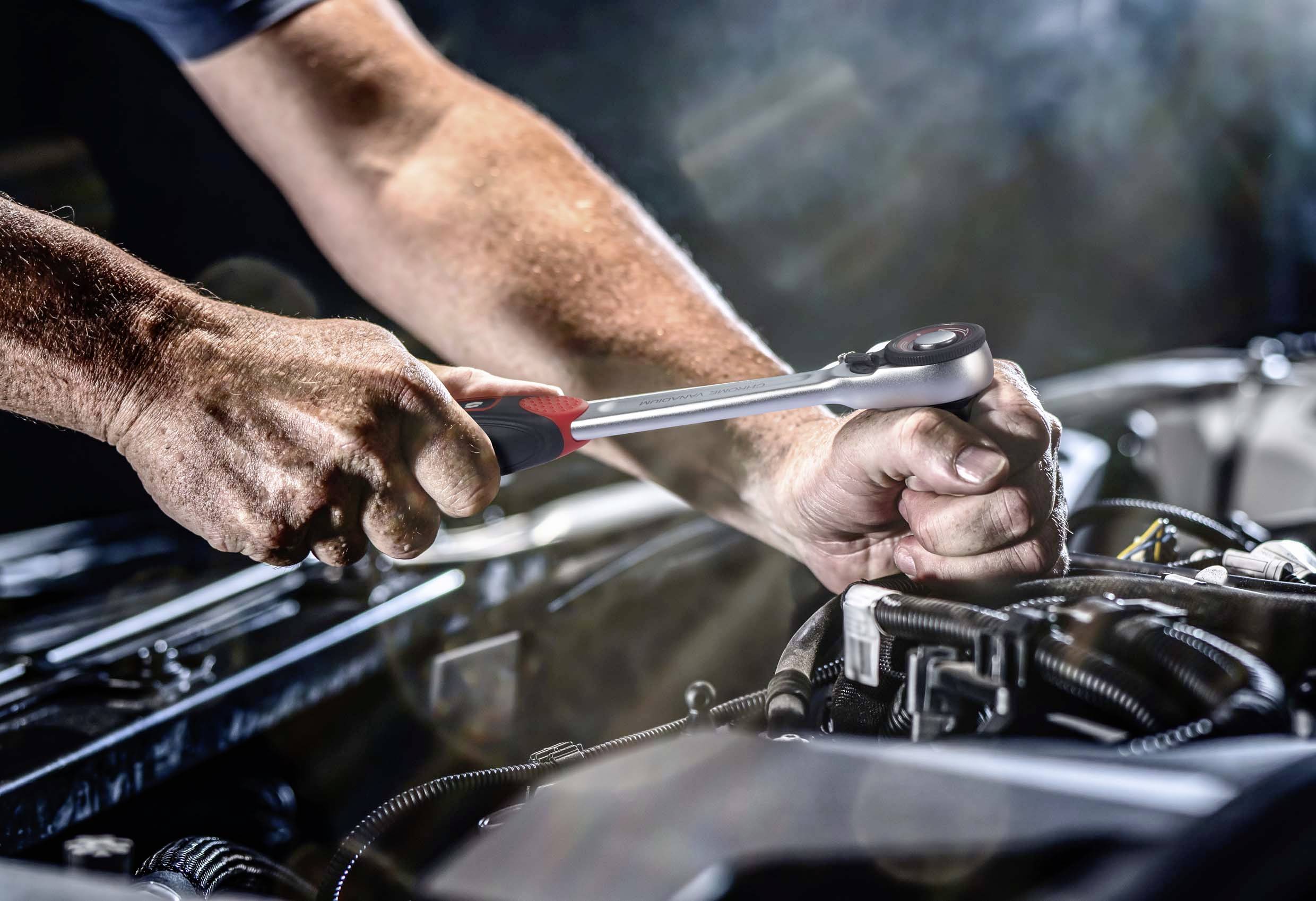 Deux mains réparent une pièce de moteur à l'aide d'une clé à molette. L'environnement est un atelier, avec l'accent mis sur le travail de réparation.