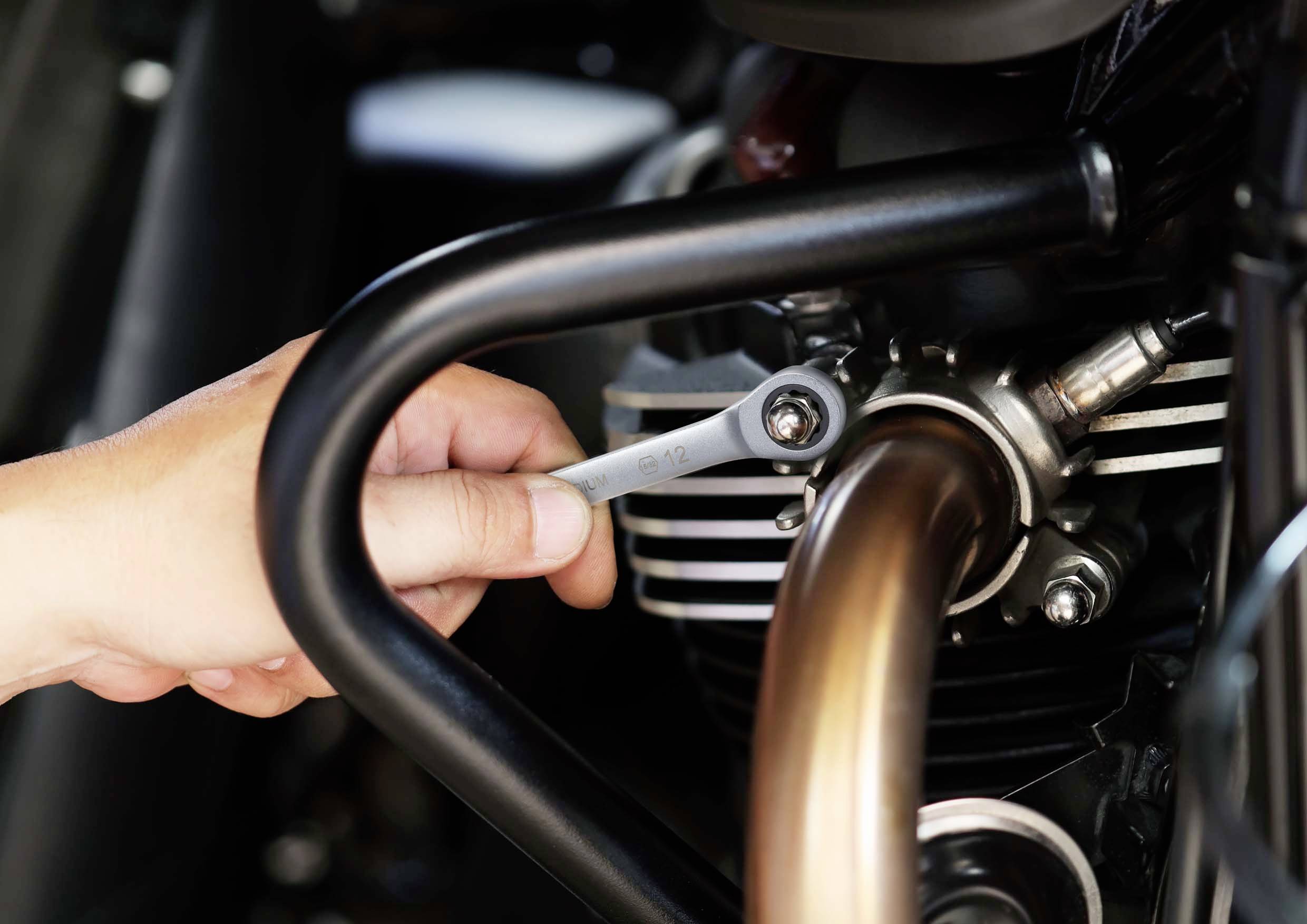 Une main tient une clé à molette et serre une vis sur le pot d'échappement d'une moto.