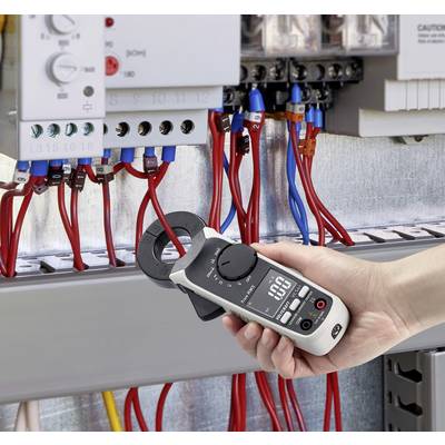 Une personne tient un multimètre numérique devant un armoire électrique ouverte, mesurant des valeurs de courant avec des câbles de connexion rouges et bleus.