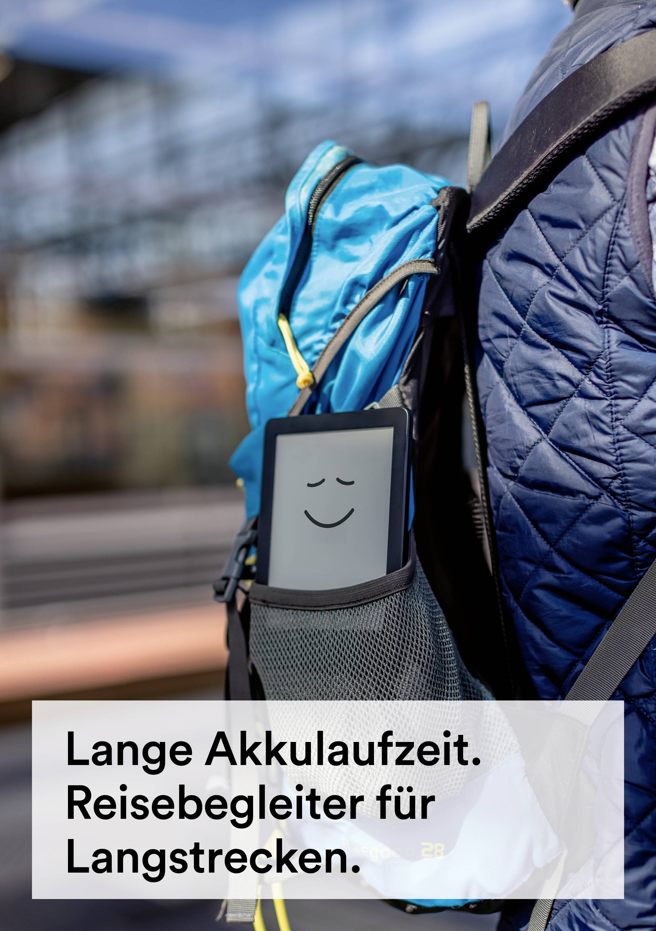 Un appareil électronique gris avec un visage souriant est coincé dans la poche latérale en filet d'un sac à dos. Texte en bas : « Longue durée de batterie. Compagnon de voyage pour longs trajets. »