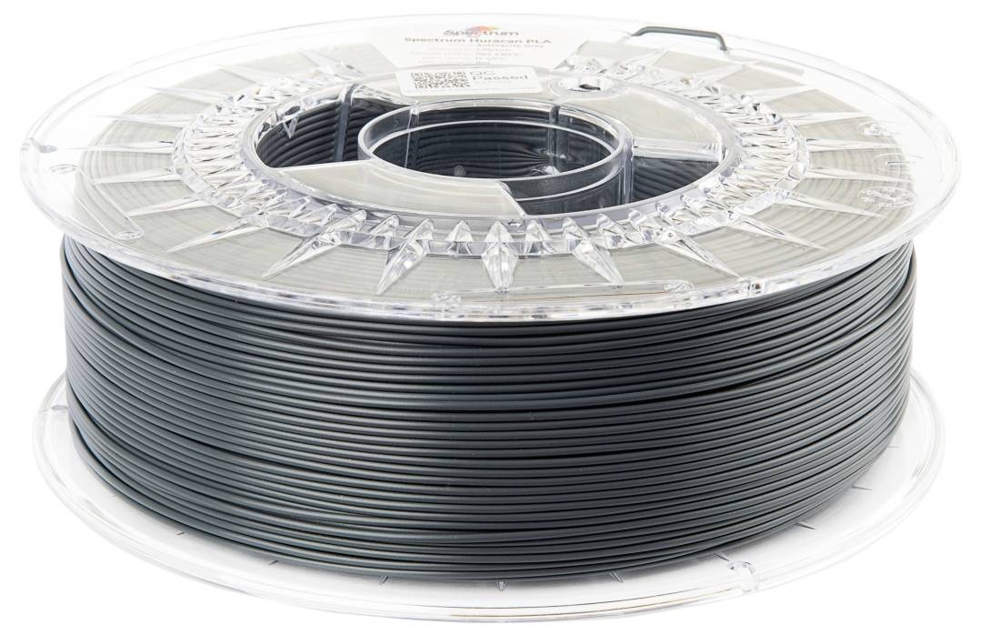 Un rouleau de filament gris foncé pour imprimante 3D, enroulé sur un support transparent.