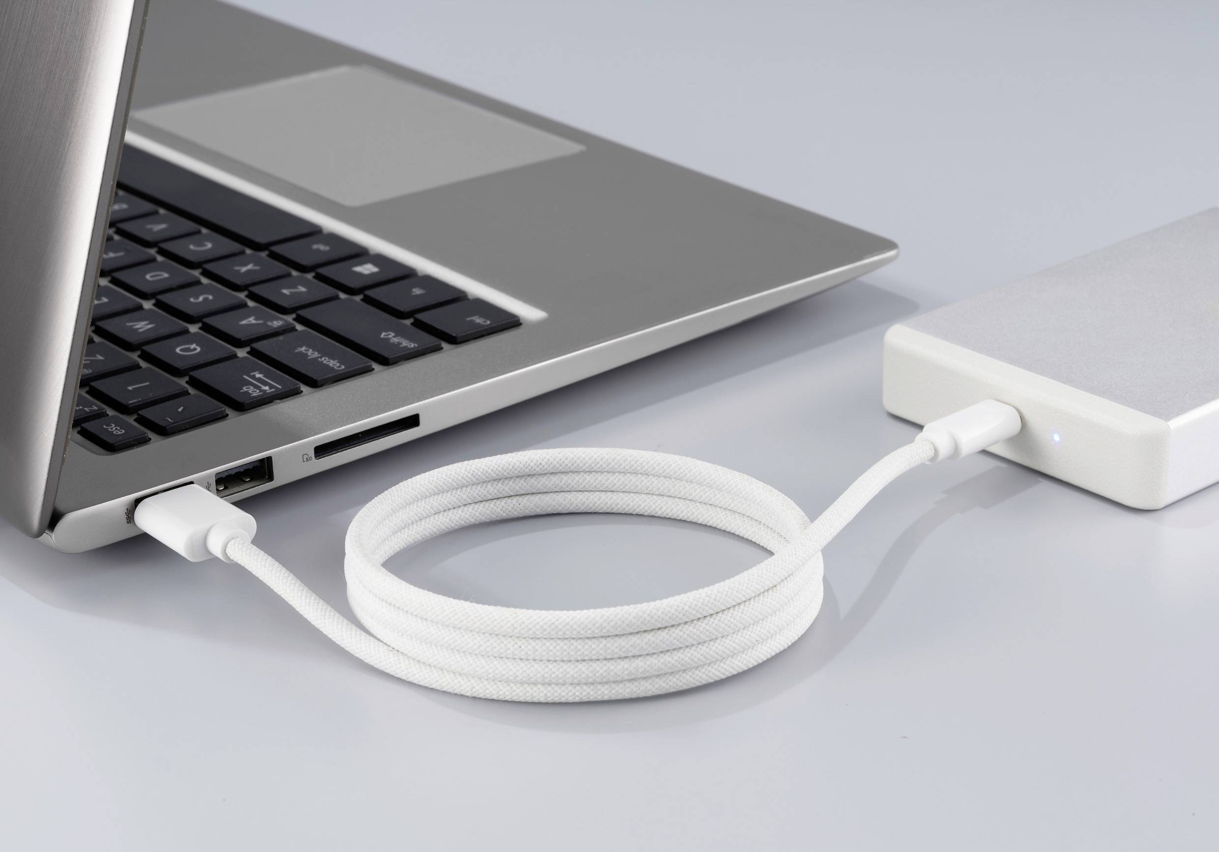 Un ordinateur portable est connecté à un disque dur externe via un câble USB tressé blanc.