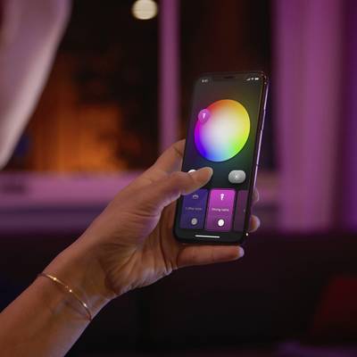 Une main tient un smartphone avec une application de contrôle des paramètres de couleur et d'éclairage. Une lumière violette en arrière-plan.
