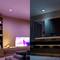 Salon avec canapé et télévision allumée à gauche ; salle de bain avec miroir et serviettes à droite. Éclairage différent.