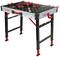 La table de travail est noire avec des accents rouges, des pieds réglables et des supports profilés, idéale pour des travaux d'atelier polyvalents.