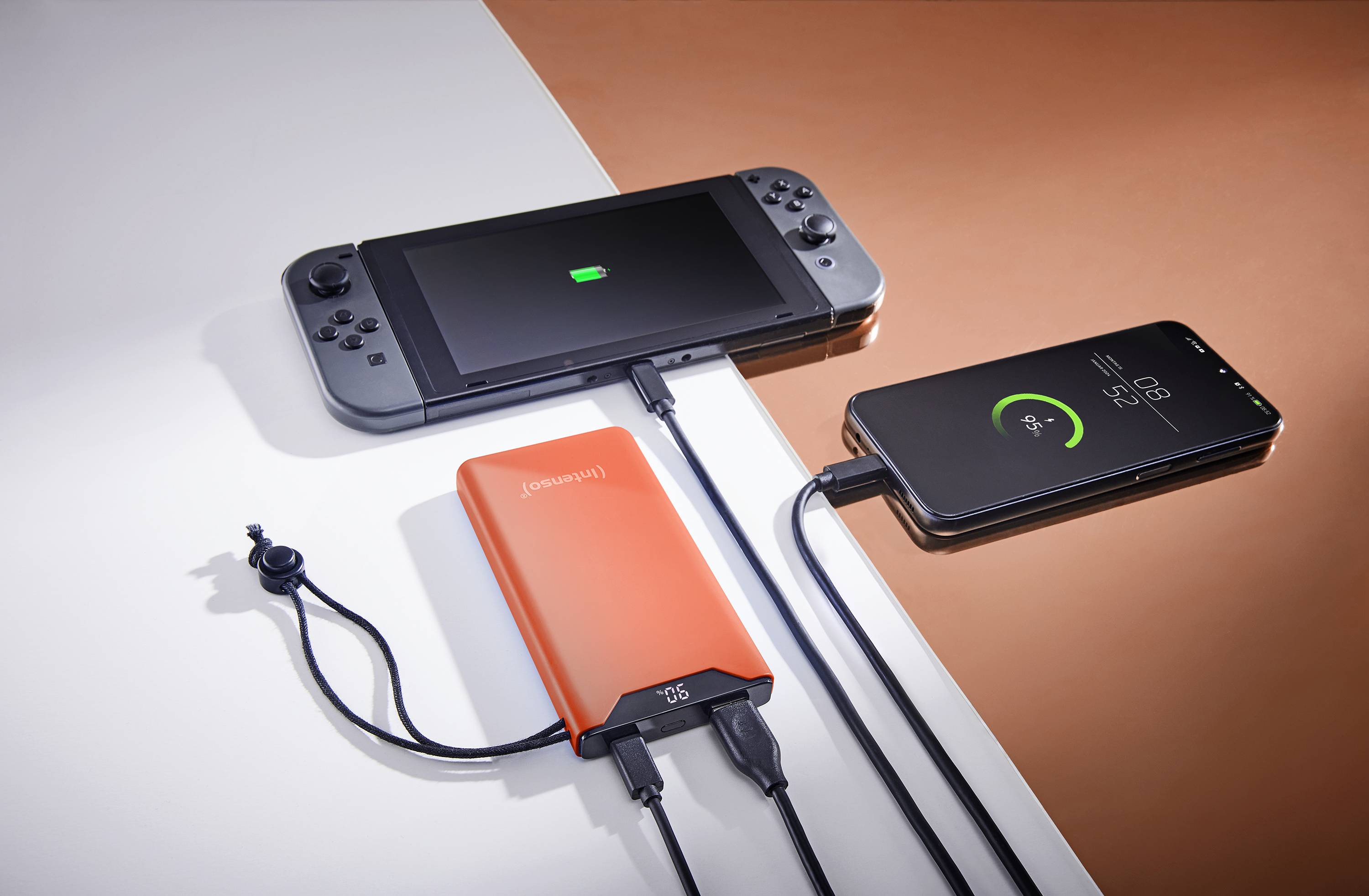 Une batterie externe charge simultanément une console de jeux portable et un smartphone. Les deux appareils affichent leur état de charge sur leur écran.