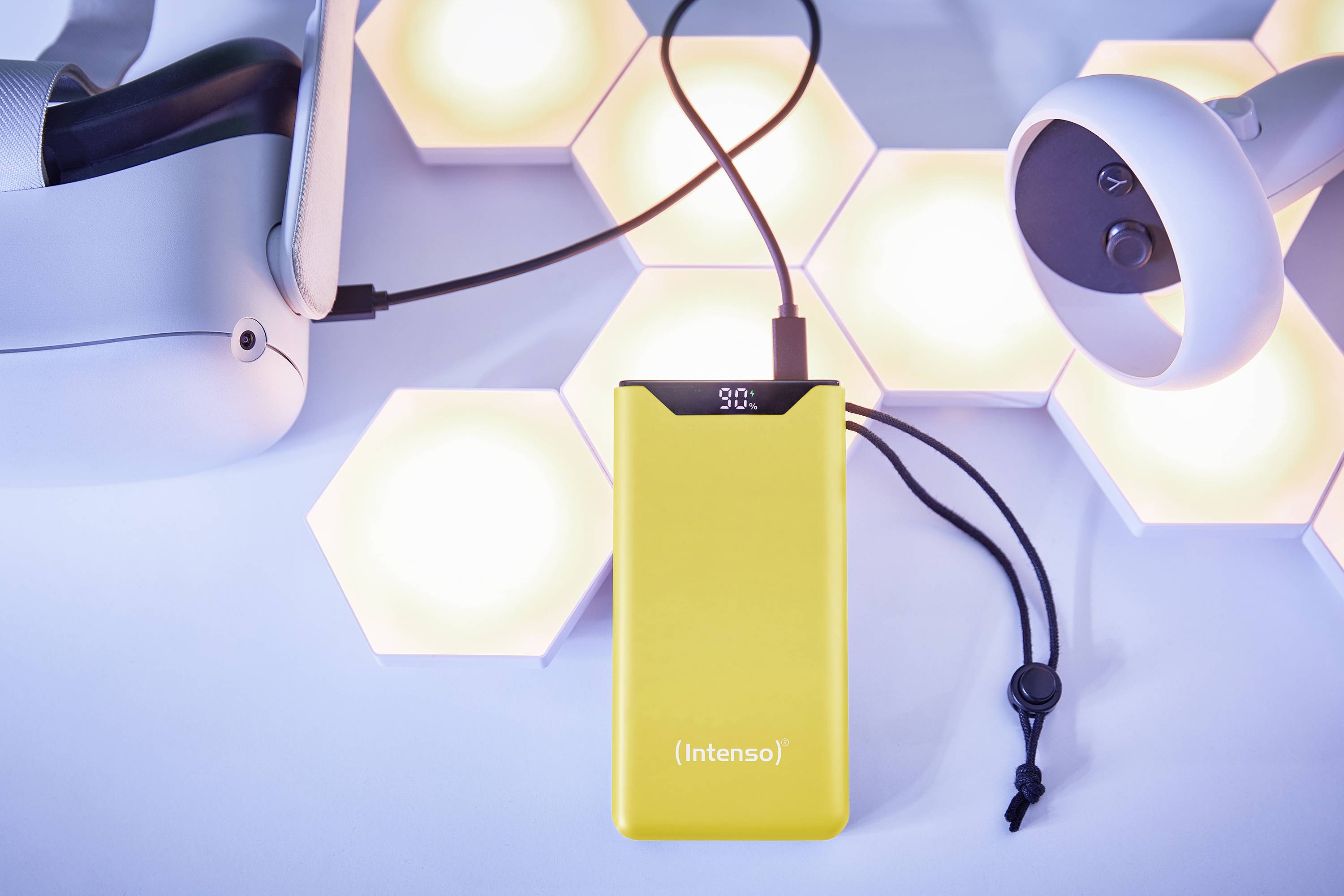 Chargeur jaune Intenso avec câble à côté d'un casque de réalité virtuelle devant des hexagones lumineux sur un fond bleu.