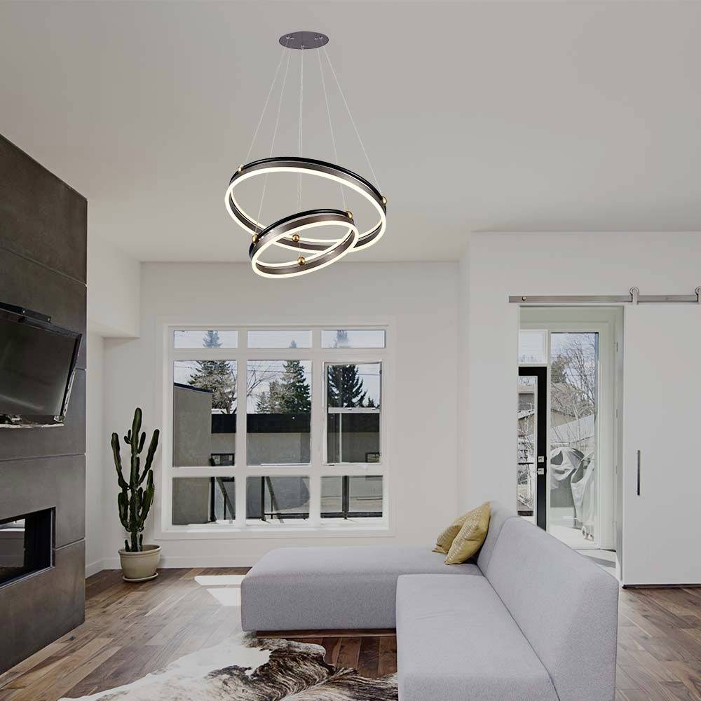 Un salon moderne avec un canapé d'angle gris, une cheminée et une suspension moderne ronde. Les fenêtres offrent une vue sur l'extérieur.