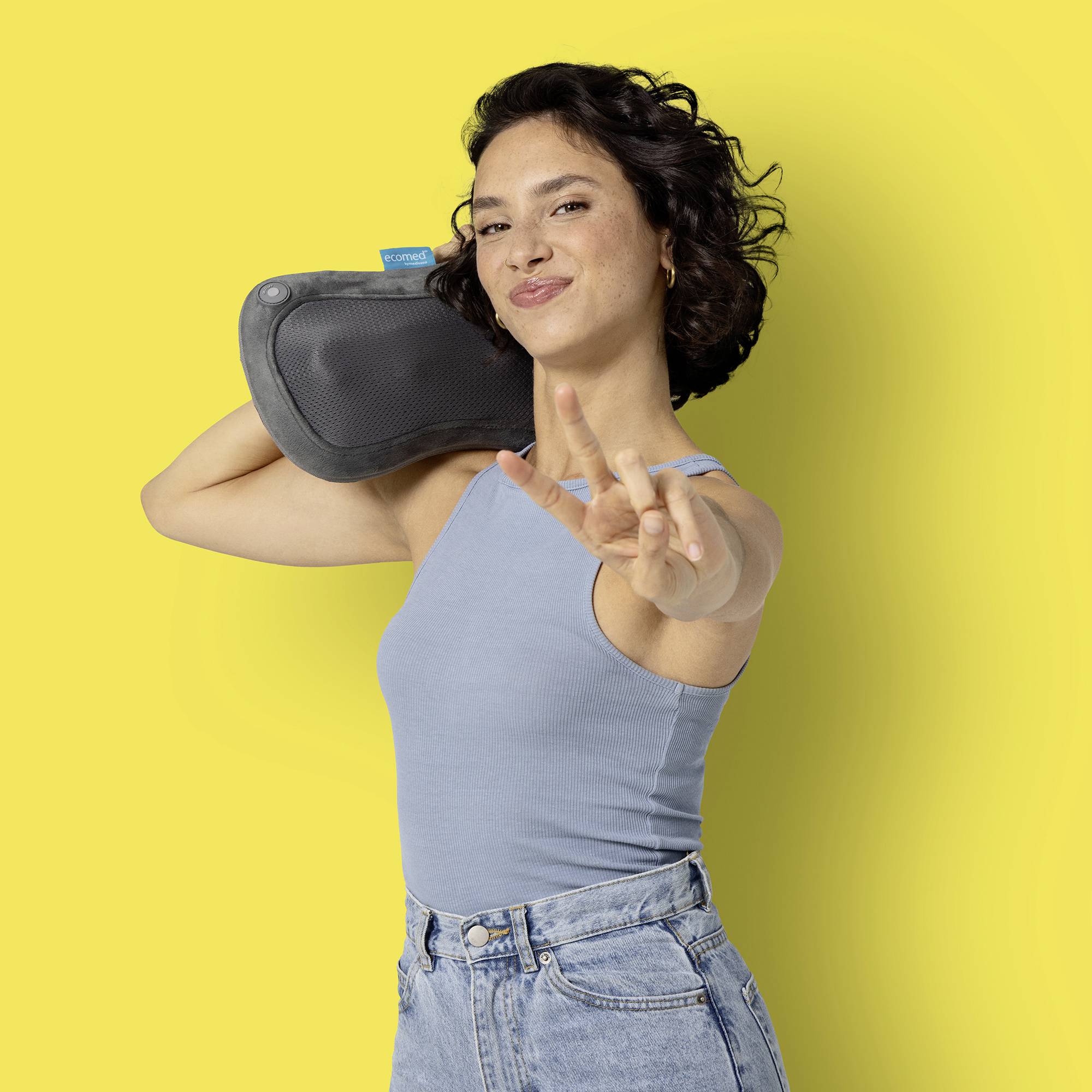 Une femme portant un haut bleu soulève une boîte portable sur son épaule et fait un signe de la main tout en souriant à la caméra.