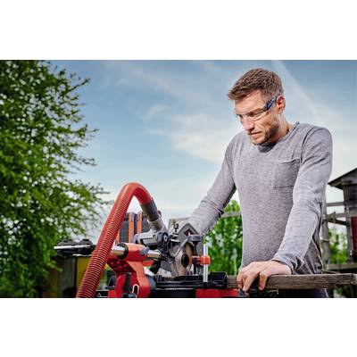 Un homme travaille avec une scie circulaire rouge à l'extérieur, porte des lunettes de protection et regarde attentivement le bois qu'il coupe.