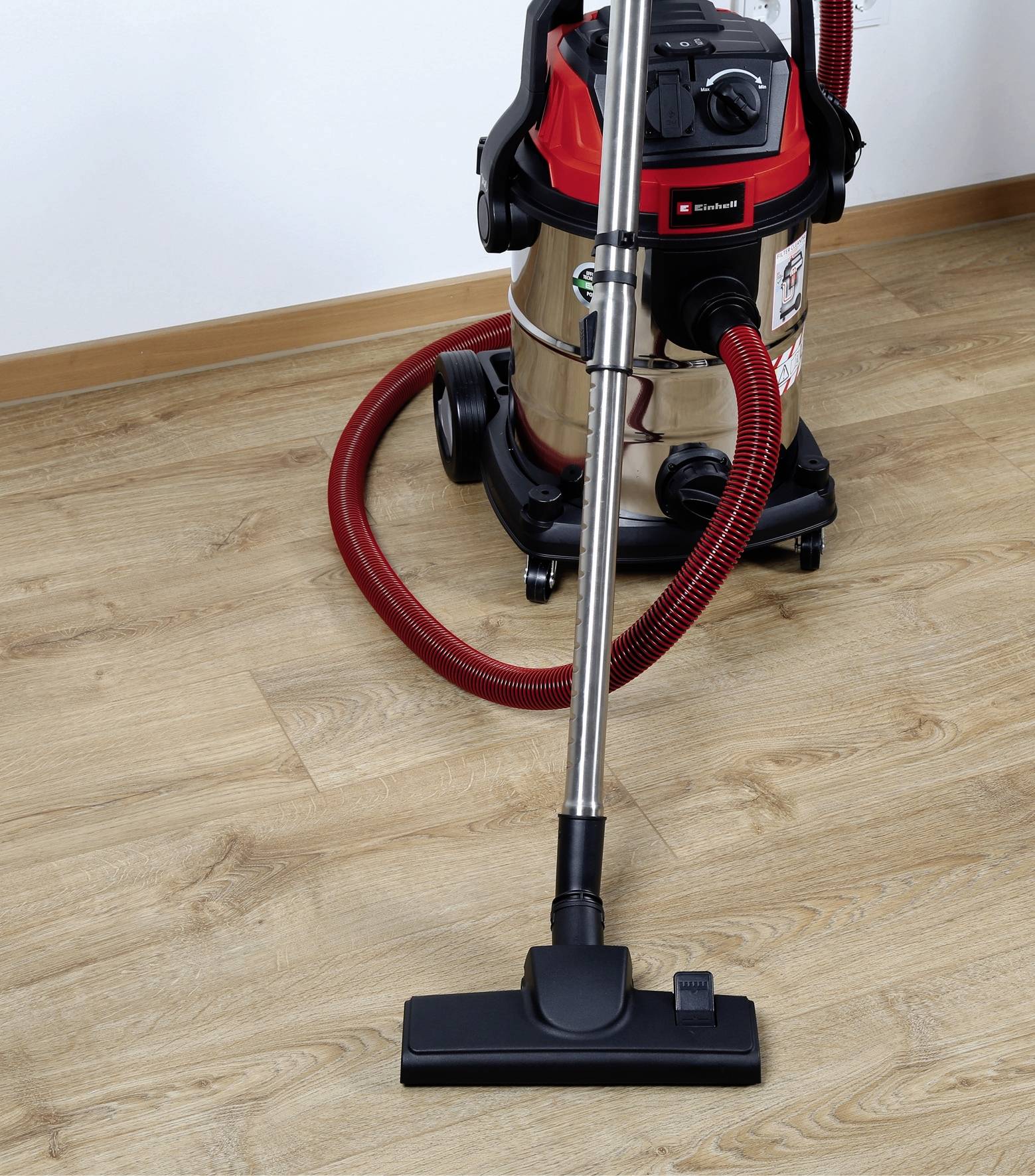 Un aspirateur puissant avec un tuyau rouge est posé sur un parquet, prêt à nettoyer.