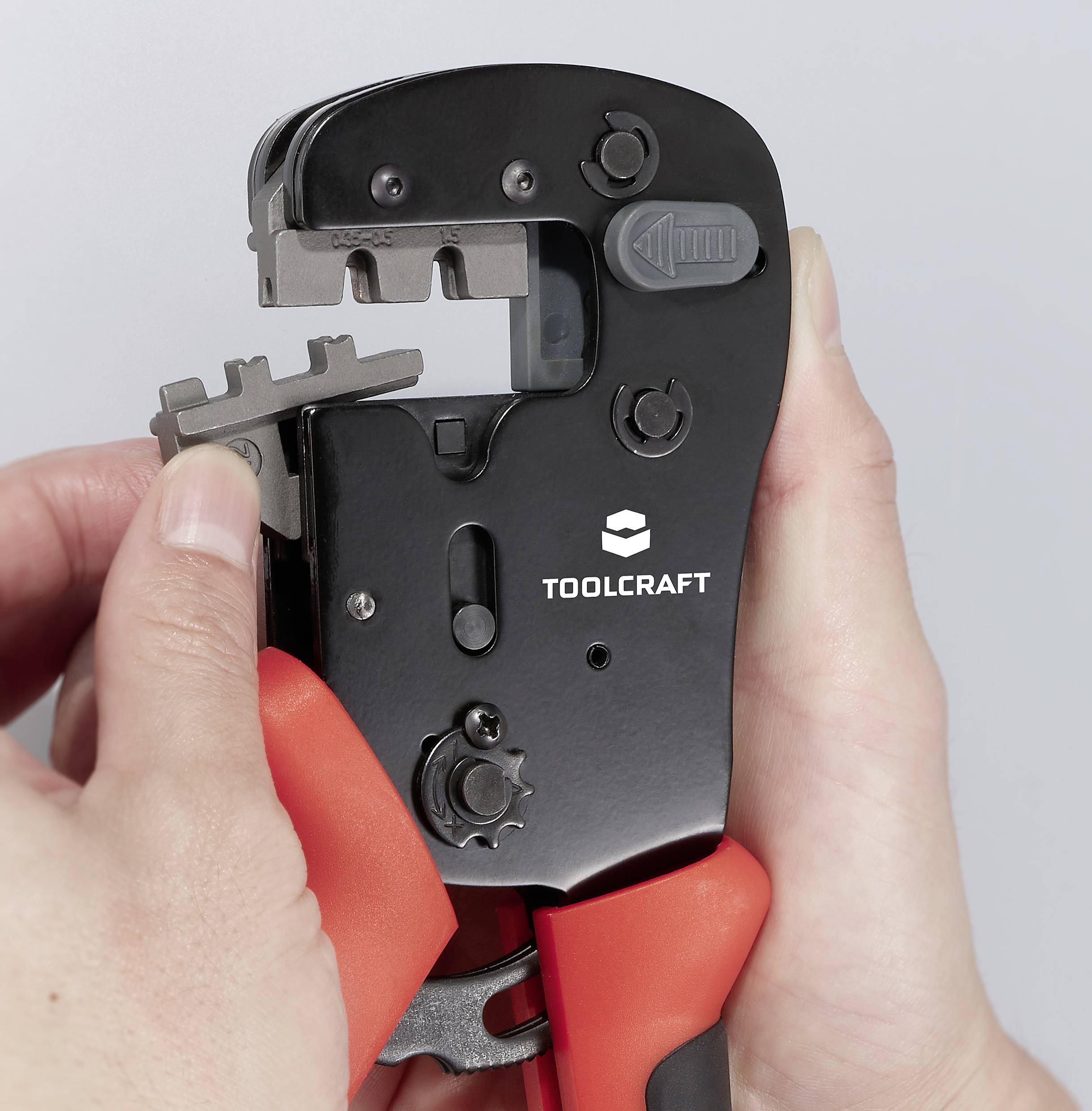 Une personne tient une pince à sertir de la marque Toolcraft, prête à sertir un câble, en gros plan.