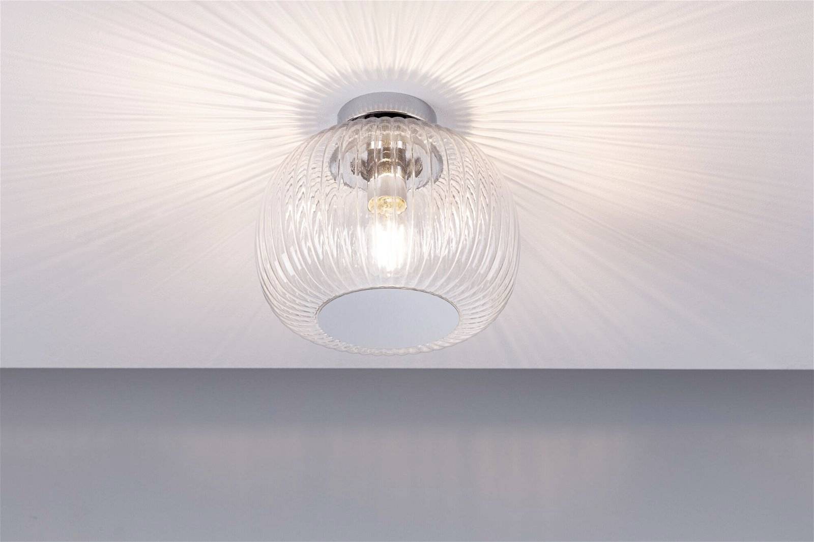 Plafonnier en verre transparent et strié, projetant un joli motif lumineux sur le plafond.