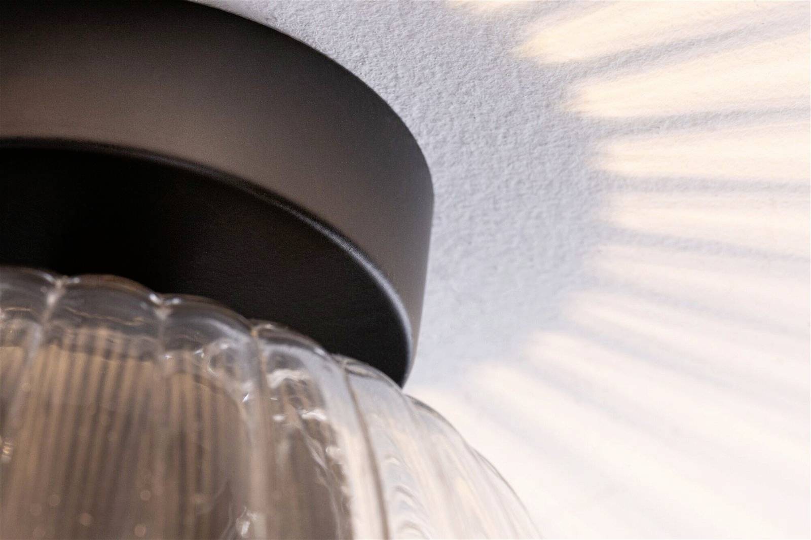 Plafonnier rond avec un abat-jour vitreux, projetant des rayons lumineux uniformes sur le plafond blanc, créant une ambiance moderne.