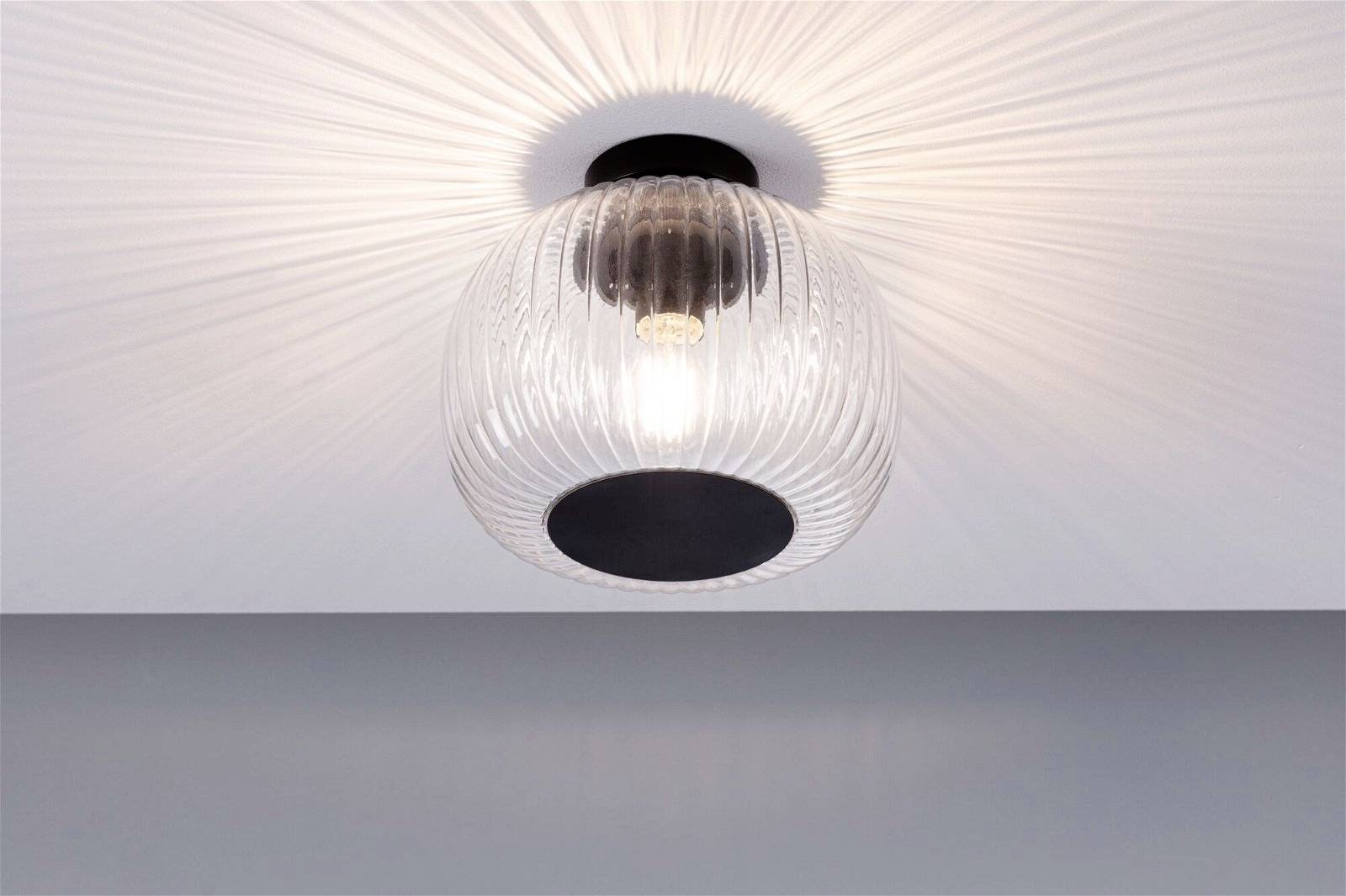 Gros plan sur un plafonnier moderne avec un corps en verre strié et une ampoule visible. Elle diffuse une lumière douce dans la pièce.