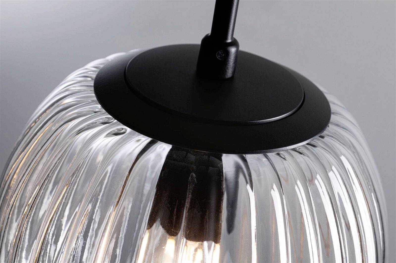 Suspension avec corps en verre strié et socle noir, illuminée avec un filament apparent.