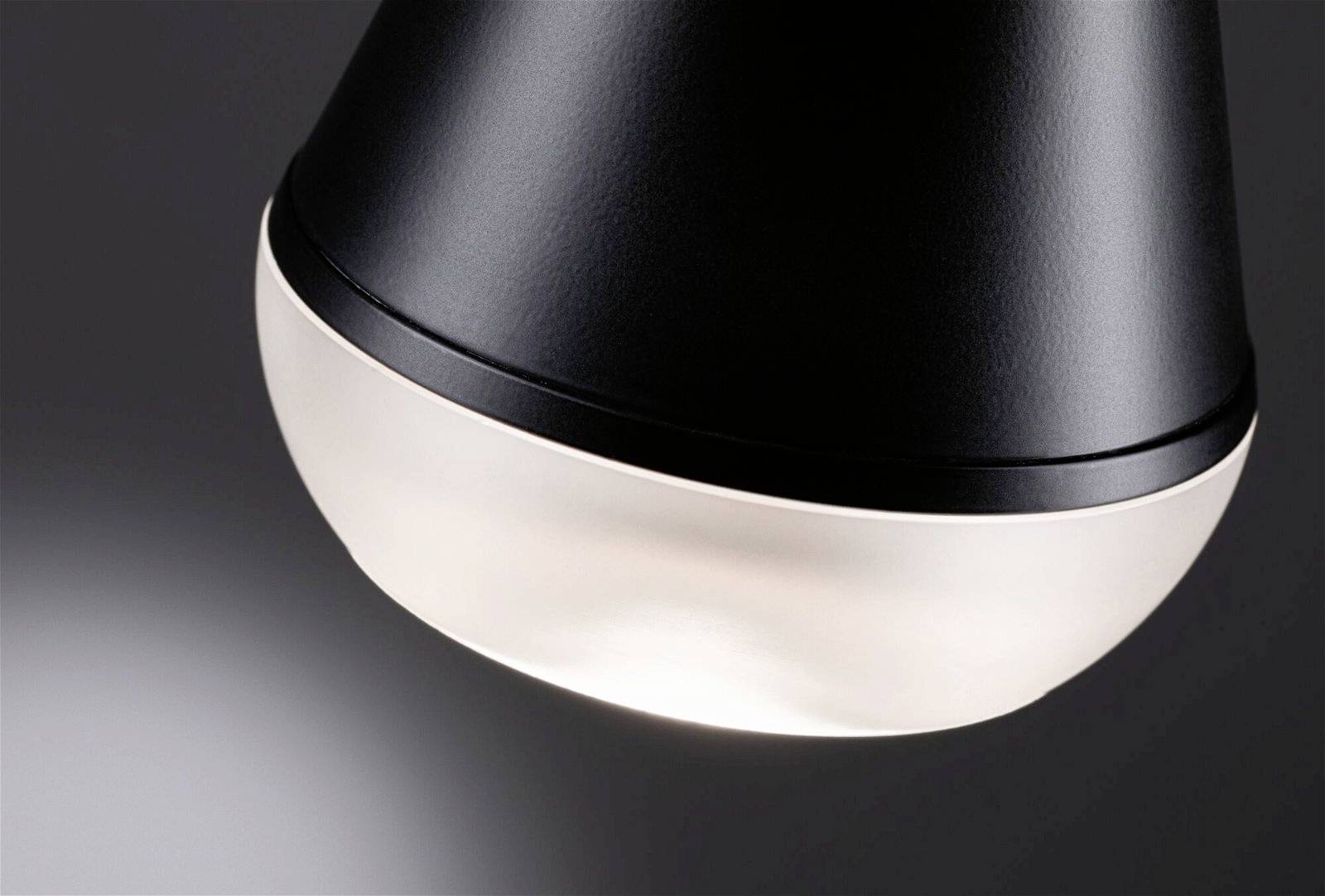 Une lampe noire au design moderne s'illumine sur un fond gris. L'accent est mis sur la face inférieure éclairée de la lampe.