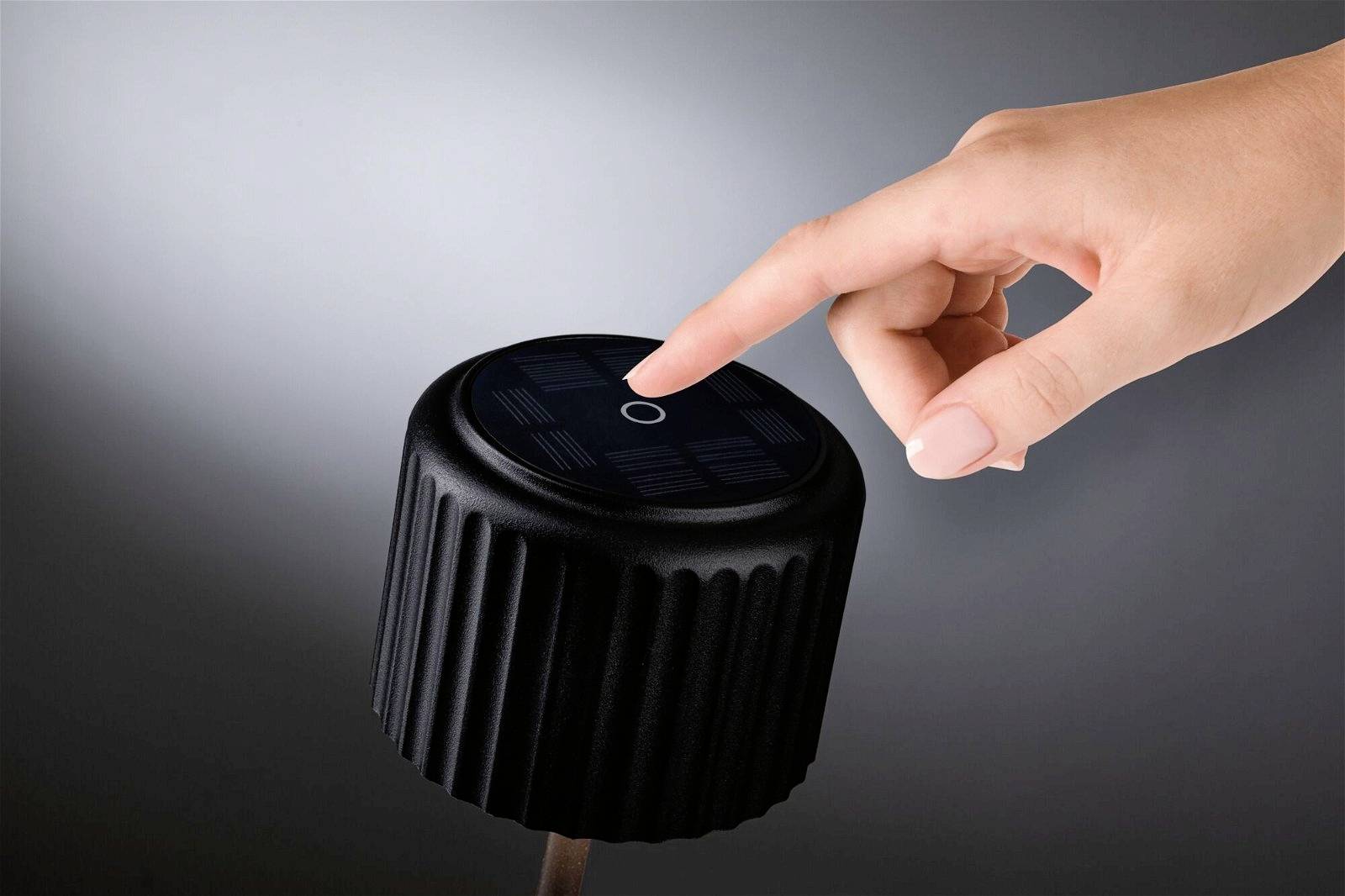 Un doigt touche un interrupteur lumineux moderne, rond, avec un boîtier noir brillant ; l'arrière-plan est gris.