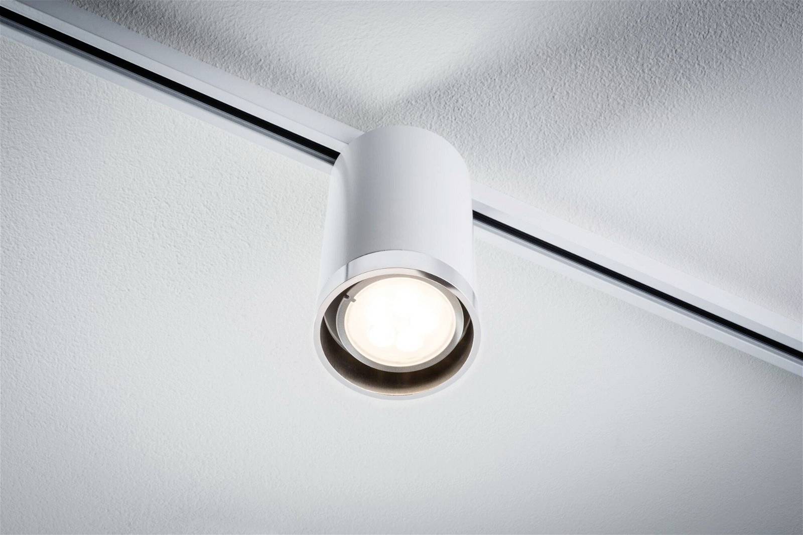 Un luminaire de plafond unique, rond, au design moderne, éclaire doucement depuis le haut. Il est fixé sur un rail.