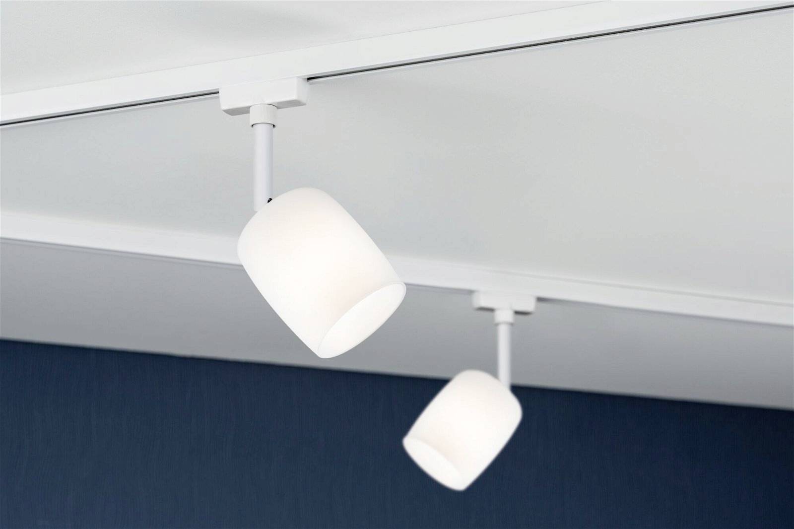 Deux spots de plafond blancs au design épuré et moderne sont montés sur un rail et illuminent une pièce.