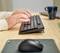 Un ordinateur portable affiche un clavier partiellement ouvert dans un bureau, la main d'une personne utilise le pavé tactile, avec un focus sur le clavier et les doigts.