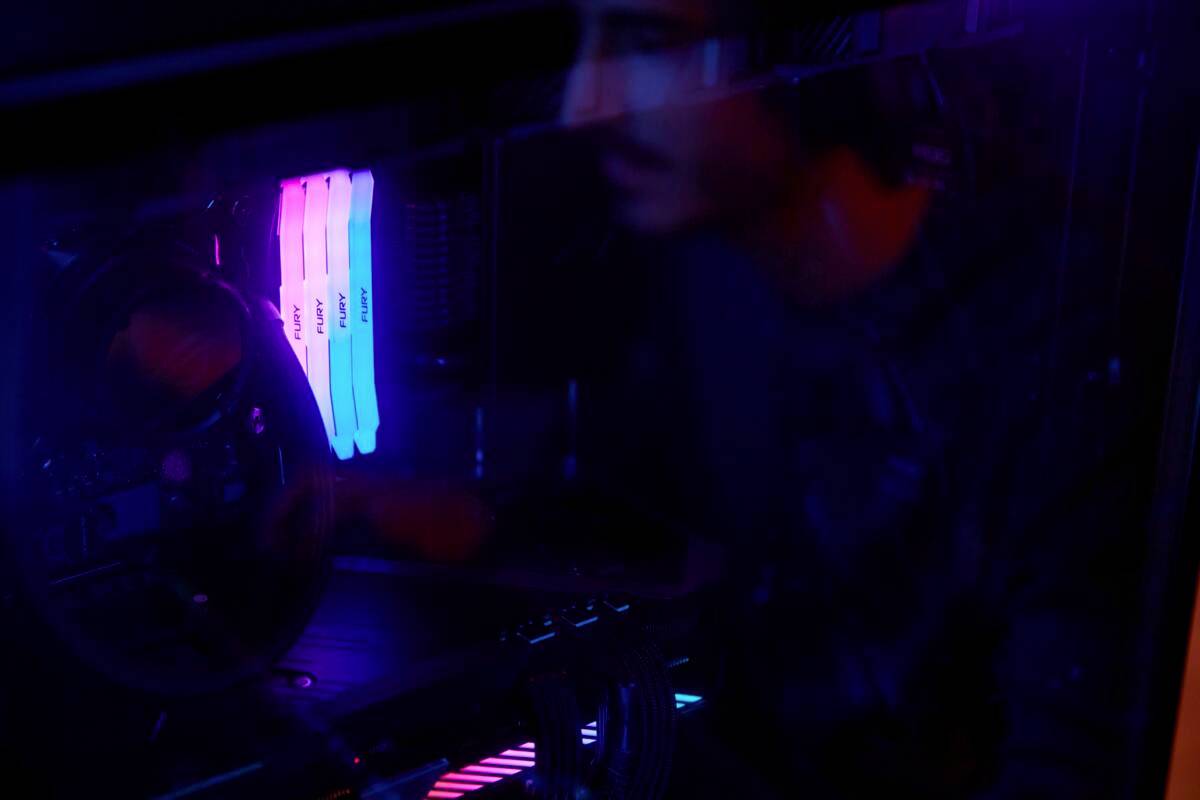 Une personne se reflète dans la fenêtre latérale d'un boîtier d'ordinateur éclairé avec des LED RVB. Les lumières sont bleues et roses.