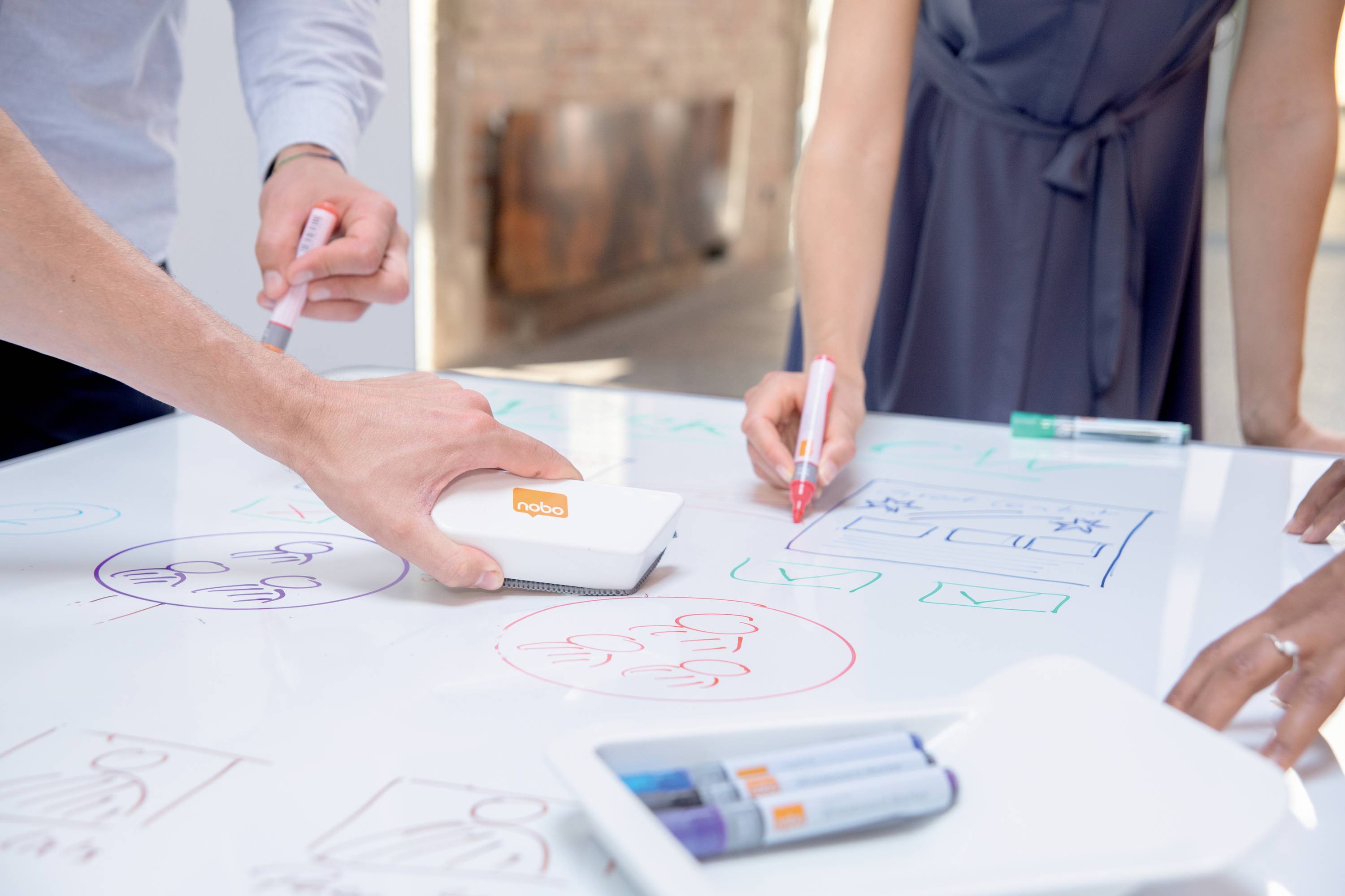 Des personnes dessinent des diagrammes et des plans sur une table blanche avec des marqueurs colorés et une gomme. Scène créative de travail d'équipe.