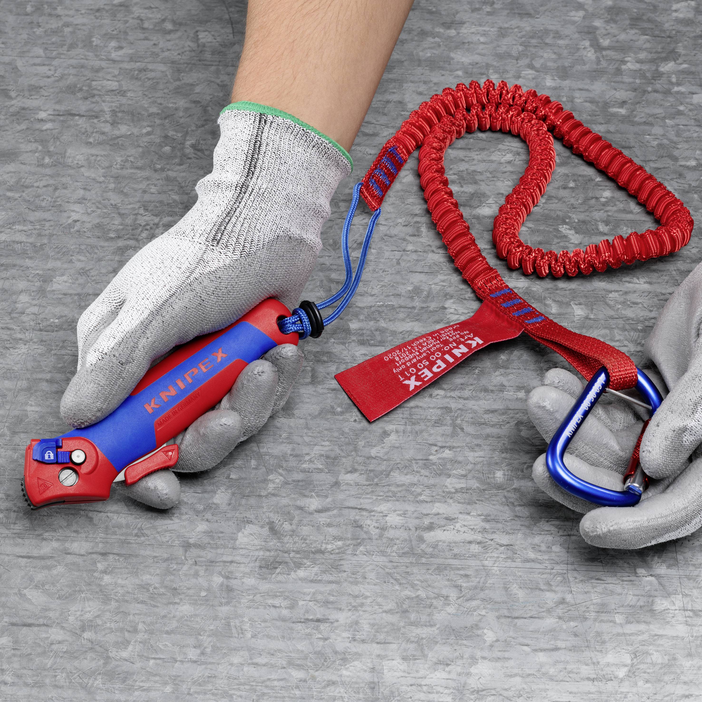 Une main portant des gants de travail tient une clé à molette rouge isolée. Une lanière de sécurité rouge est attachée à l'outil.